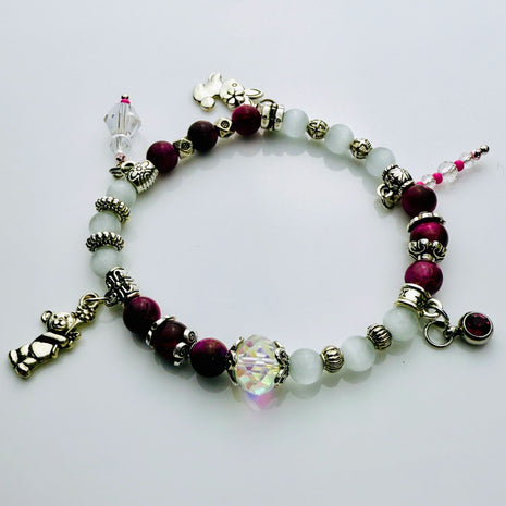 Verspieltes Damenarmband mit Anhängern wie Teddybär, Blüten und Schmuckelementen, kombiniert mit weißen und weinroten Perlen, ideal als verspieltes Accessoire.