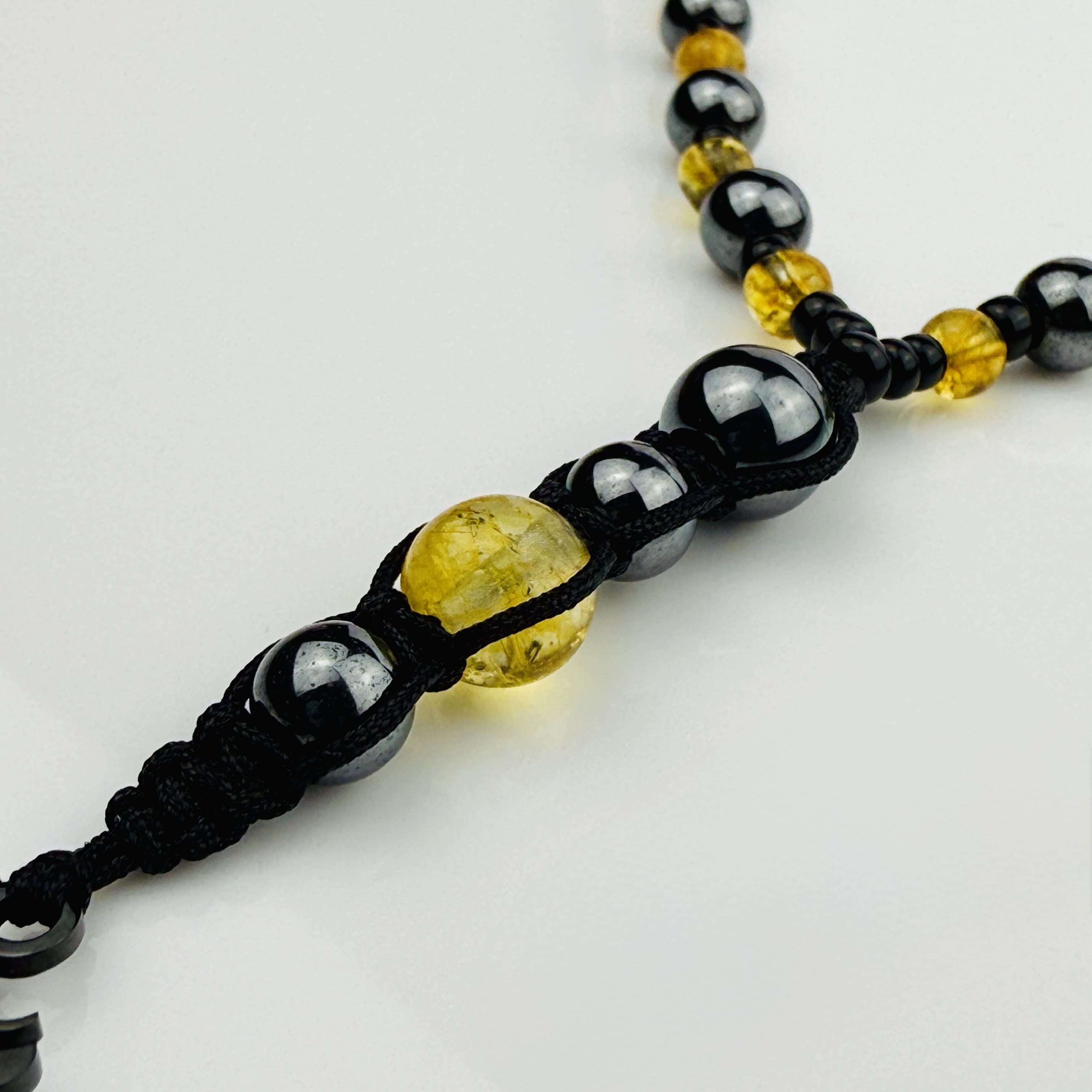 Handgefertigte Y-Halskette für Herren mit gelbem Citrin, Hämatit-Perlen und einem eleganten Edelstahl-Federnanhänger. Kunstvolle Makramee-Technik und schwarze Rocailles ergänzen das moderne und stilvolle Design.