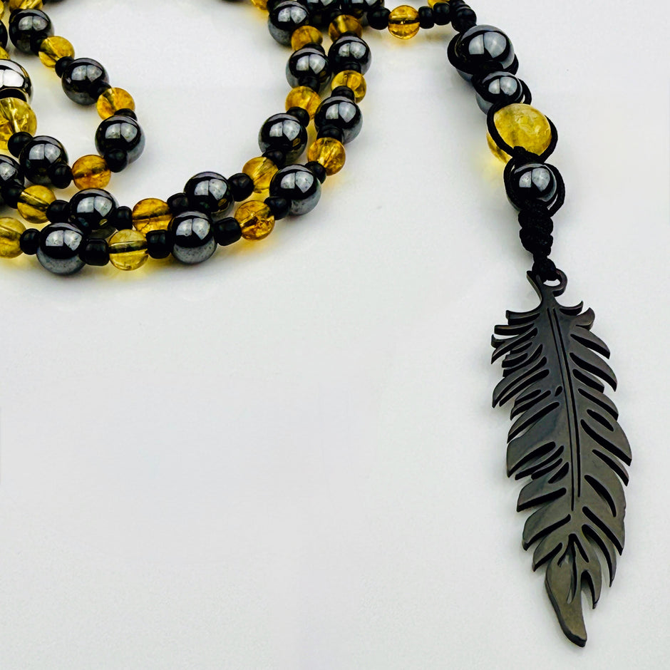 Handgefertigte Y-Halskette für Herren mit gelbem Citrin, Hämatit-Perlen und einem eleganten Edelstahl-Federnanhänger. Kunstvolle Makramee-Technik und schwarze Rocailles ergänzen das moderne und stilvolle Design.