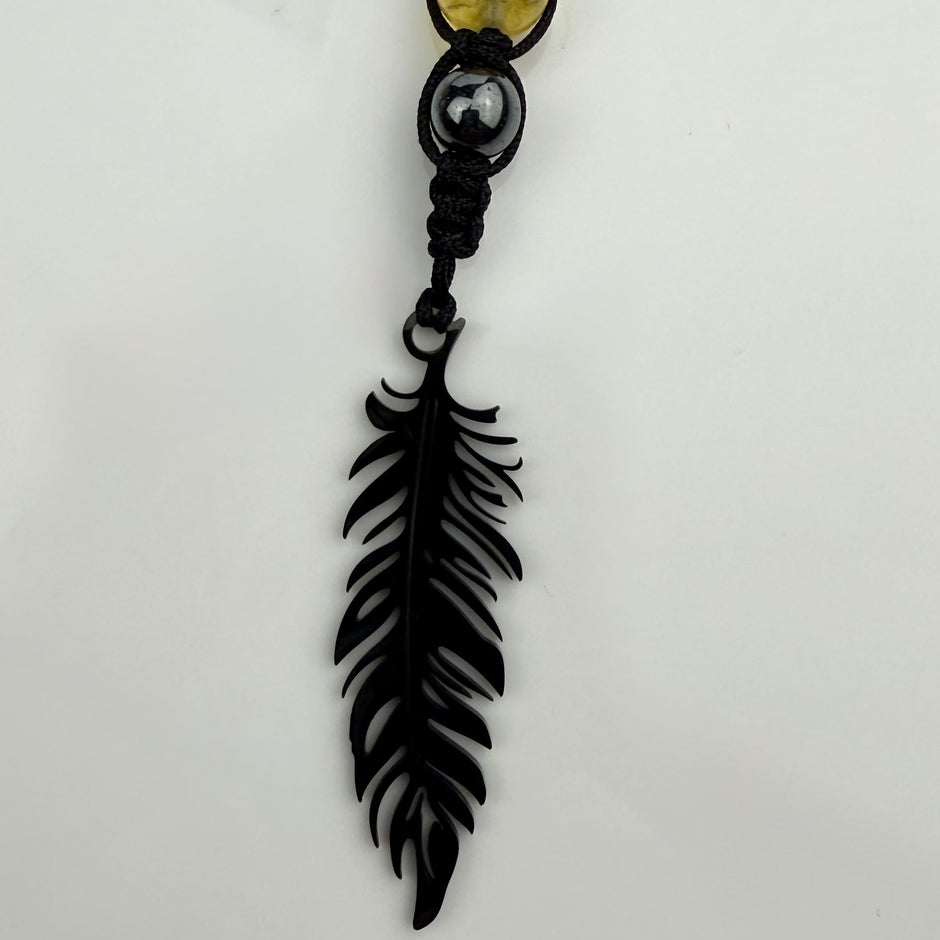 Handgefertigte Y-Halskette für Herren mit gelbem Citrin, Hämatit-Perlen und einem eleganten Edelstahl-Federnanhänger. Kunstvolle Makramee-Technik und schwarze Rocailles ergänzen das moderne und stilvolle Design.