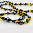 Handgefertigte Y-Halskette für Herren mit gelbem Citrin, Hämatit-Perlen und einem eleganten Edelstahl-Federnanhänger. Kunstvolle Makramee-Technik und schwarze Rocailles ergänzen das moderne und stilvolle Design.