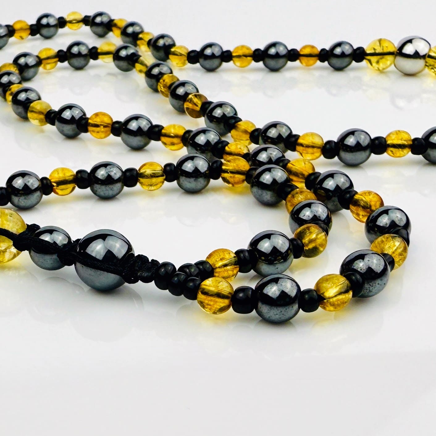 Handgefertigte Y-Halskette für Herren mit gelbem Citrin, Hämatit-Perlen und einem eleganten Edelstahl-Federnanhänger. Kunstvolle Makramee-Technik und schwarze Rocailles ergänzen das moderne und stilvolle Design.