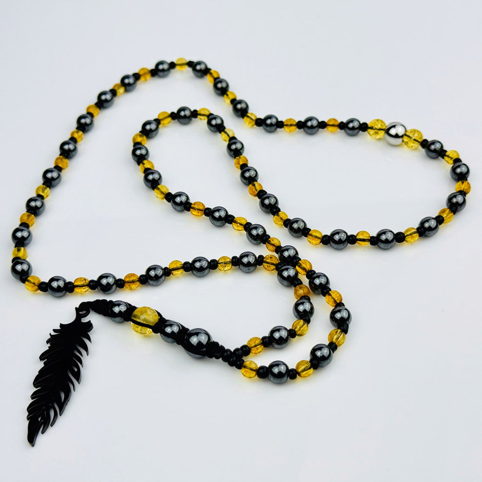 Handgefertigte Y-Halskette für Herren mit gelbem Citrin, Hämatit-Perlen und einem eleganten Edelstahl-Federnanhänger. Kunstvolle Makramee-Technik und schwarze Rocailles ergänzen das moderne und stilvolle Design.