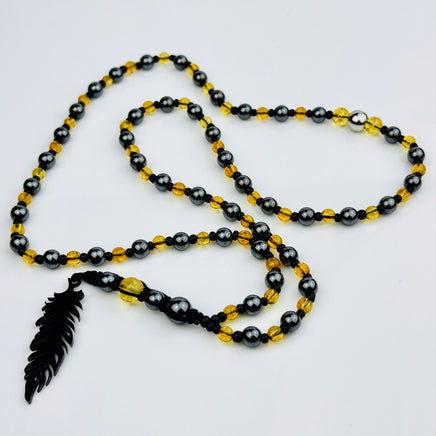 Handgefertigte Y-Halskette für Herren mit gelbem Citrin, Hämatit-Perlen und einem eleganten Edelstahl-Federnanhänger. Kunstvolle Makramee-Technik und schwarze Rocailles ergänzen das moderne und stilvolle Design.