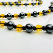 Handgefertigte Y-Halskette für Herren mit gelbem Citrin, Hämatit-Perlen und einem eleganten Edelstahl-Federnanhänger. Kunstvolle Makramee-Technik und schwarze Rocailles ergänzen das moderne und stilvolle Design.