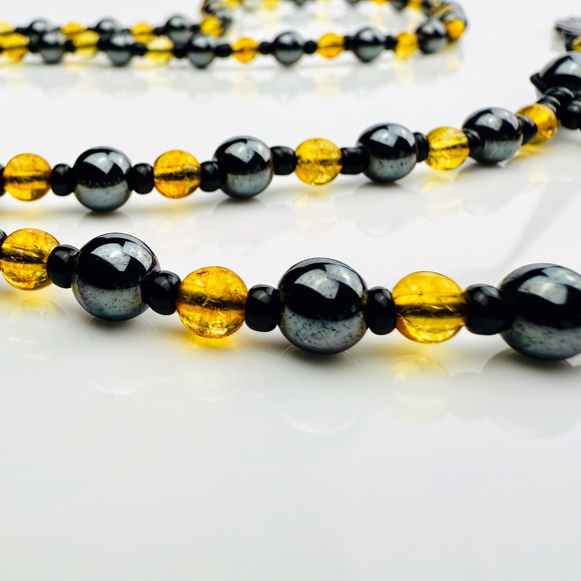 Handgefertigte Y-Halskette für Herren mit gelbem Citrin, Hämatit-Perlen und einem eleganten Edelstahl-Federnanhänger. Kunstvolle Makramee-Technik und schwarze Rocailles ergänzen das moderne und stilvolle Design.