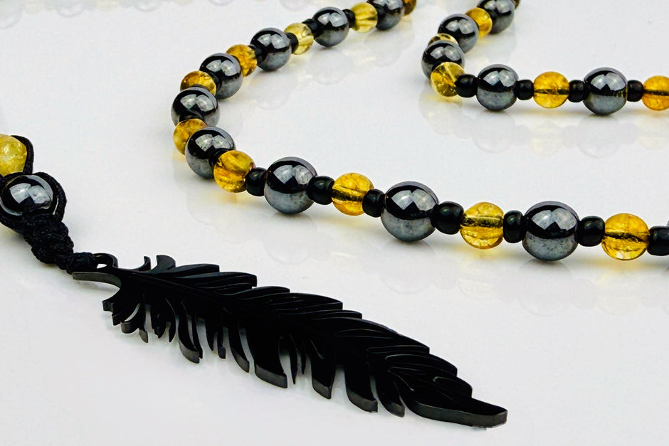 Handgefertigte Y-Halskette für Herren mit gelbem Citrin, Hämatit-Perlen und einem eleganten Edelstahl-Federnanhänger. Kunstvolle Makramee-Technik und schwarze Rocailles ergänzen das moderne und stilvolle Design.
